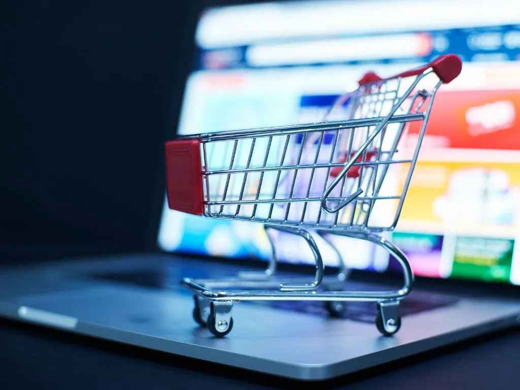 a physical cart on a laptop with blurred screen showing the concept of ecommerce